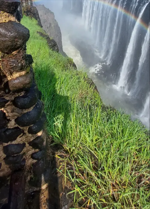 Rainbow over the Victoria Falls gorge seen from a grassy cliff path